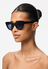 Mustat kissansilmäaurinkolasit tummilla linssillä, kulmikas muotoilu ja paksut kehykset. Tasainen muovimateriaali luo tyylikkään ilmeen.
