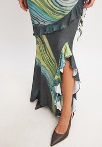 Printed dress featuring a swirling green and blue design, with a ruffled hemline and a side slit. Paired with brown pointed-toe heels.