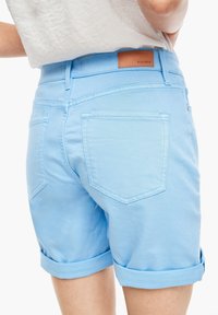 Personne portant un short en denim bleu clair retroussé avec des poches arrière et une étiquette brune S.Oliver sur la ceinture.