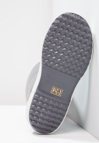 Semelle de chaussure en caoutchouc avec un motif texturé gris, comportant une section rectangulaire en gris uni avec le numéro "28" en surbrillance dorée.