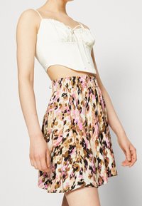 Top corto bianco con chiusura a lacci abbinato a una gonna a fiori nei colori rosa, marrone e nero, dotata di una cintura elastica.