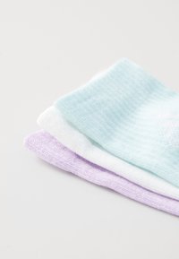 Tre par med sokker i pastellfarger: lys mintgrønn, hvit og lavendel. Hver sokk har et mykt, strukturert strikkedesign.