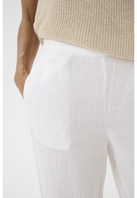 Witte linnen broek met een ontspannen pasvorm en een subtiele textuur, voorzien van zijzakken en een elastische tailleband voor comfort.