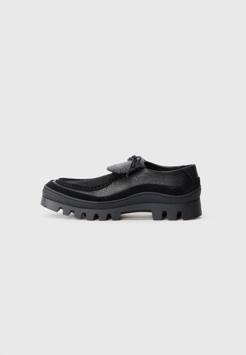 Black casual shoes featuring a textured leather upper, rounded toe, and a sturdy lug sole for traction. Decorative lacing detail at the front.