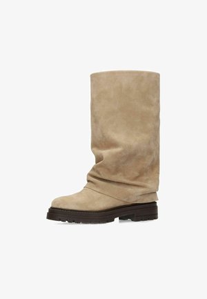 Beige suède midkuitlaars met losse schacht, afgeronde neus en dikke donkerbruine rubberen profielzool.