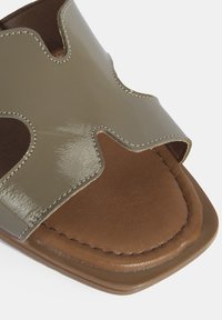 Tong sandale en patin kaki avec une conception à bout ouvert, semelle intérieure marron contrastante et coutures décoratives sur les bords.