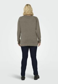 Pull à manches longues vert olive avec un ourlet côtelé, coupe décontractée et encolure ras du cou, associé à un jean bleu foncé et des chaussures noires.