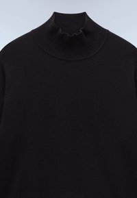 Mustavilla turtleneck-pusero, joka on valmistettu pehmeästä neuloksesta. Ominaisuuksiin kuuluu ribbireunus, jossa on kerroksellista yksityiskohtaa, sekä rento istuvuus vartalolla.