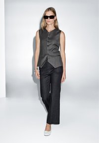 Gray sleeveless vest with a v-neck, front buttons, and two pockets, paired with dark wide-leg trousers and white slip-on shoes.