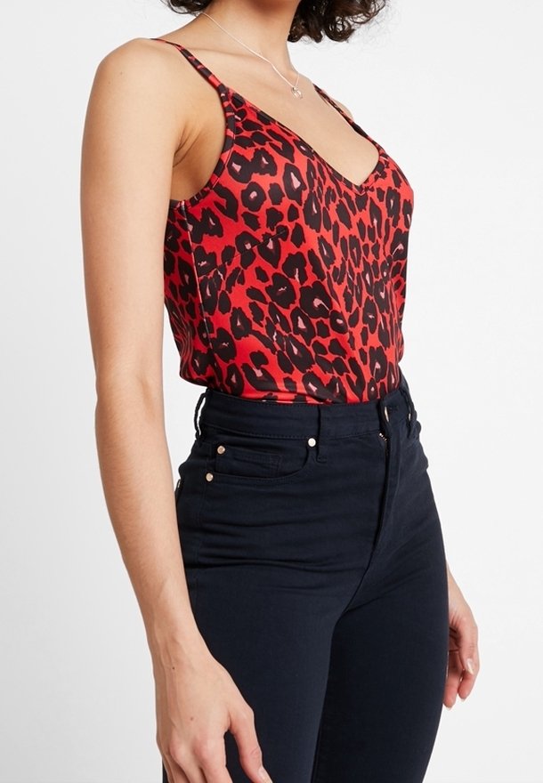 Röd och svart leopardmönstrad topp med V-ringning och tunna axelband, i kombination med högmidjade mörkblå jeans. Slitstark och stretchig tyg.