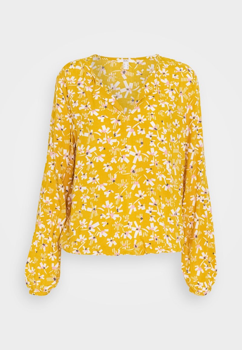 Blouse jaune à manches longues avec un col en V, présentant un motif floral en rose et blanc. Fabriquée en tissu léger avec un ourlet légèrement froncé.