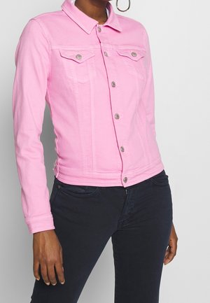 Vrouw draagt een aansluitend roze spijkerjack met knopen en klepzakken, gecombineerd met donkere high-waisted jeans, tegen een effen achtergrond.