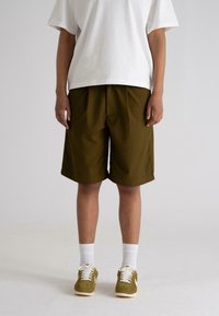 Olivenfargede shorts med avslappet passform, laget av lett stoff, kombinert med hvite sokker og brune semskede sneakers.