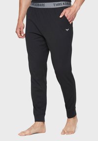 Sorte bomuldsjoggers har et gråt elastisk livbånd med "THREADBARE" branding og et lille logo. Designet inkluderer sidelommer og tapered ben.