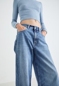 Light blue ribbed crop top paired with loose-fitting, light blue denim jeans featuring a button closure and front pockets.