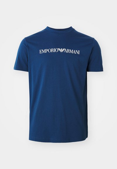 Temno modra bombažna majica s krožnim izrezom, na kateri je v beli barvi napisan logotip "EMPORIO ARMANI" čez prsi. Kratke rokave, običajen kroj.