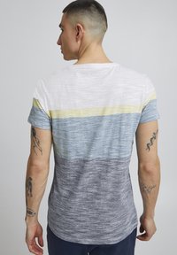 Camiseta de manga corta en rayas blancas, azules, amarillas y grises. Tejido suave con una textura combinada. Cuello redondeado y corte relajado.