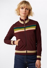 Bordeaux ritsjack met een hoge kraag, voorzien van horizontale strepen in groen, geel en rood. Inclusief zijzakken en geribde manchetten.