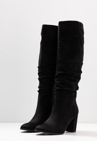 Black knee-high boots made of soft suede, featuring a gathered design and a block heel, with a pointed toe and zipper closure.