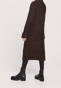 Cappotto a maglia marrone con texture, maniche lunghe, spacchi laterali e colletto alto, abbinato a stivaletti neri alla caviglia e leggings neri.