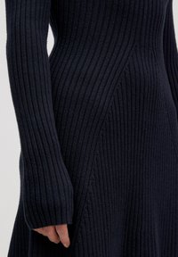 Navy-blaues Rippstrickkleid mit langen Ärmeln und asymmetrischen Seitennähten. Der Stoff ist weich, mit einem taillierten Oberteil und einer ausgestellten Silhouette.