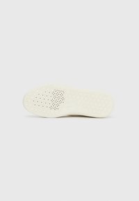 Semelle d'une chaussure beige avec des motifs hexagonaux et de petites perforations pour la respirabilité sur un fond blanc uni.