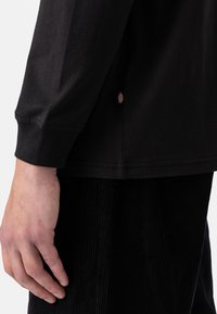 Zwarte langarmshirt van katoen, met een subtiele ribbelstructuur en een klein logo-label aan de zijkant. Zichtbare stikseldetails.