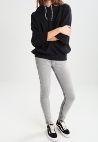 Sudadera oversized negra con cordones blancos, combinada con unos jeans ajustados grises y zapatillas negras con cordones y suela blanca.
