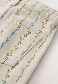 Tissu de couleur claire avec des vignes florales brodées verticalement en bleu, jaune et rouge, comportant une poche rectangulaire cousue.