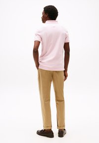 Világos rózsaszín galléros póló, bézs chino nadrággal és sötétbarna cipővel párosítva. Sima textúra, egyszerű kialakítás, látható minták nélkül.