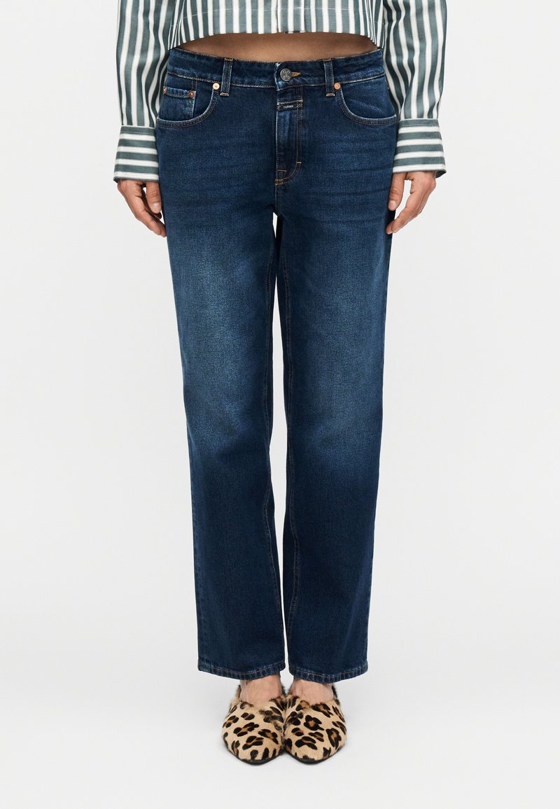 Σκούρα μπλε τζιν με ίσια εφαρμογή στα πόδια, διαθ έσιμα με παραδοσιακές τσέπες και κλείσιμο με κουμπί. Φοριούνται με παπούτσια τύπου slip-on με λεοπάρ σχέδιο.