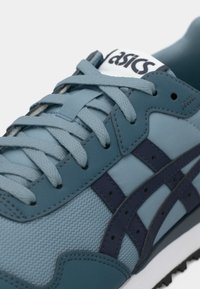 Világoskék sportcipő, hálós és szintetikus anyagból, sötétkék részletekkel és fűzőkkel, megerősített fűzőlyukakkal és textúrázott mintával.