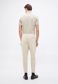 Beżowa koszulka polo z krótkimi rękawami, w połączeniu z jasnobeżowymi dresami z elastycznym pasem i dwoma bocznymi kieszeniami, noszona z czarnymi butami.