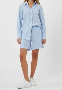 Ensemble chemise et short en coton rayé bleu et blanc. La chemise est à boutons, manches longues ; le short est ample. Porté avec des baskets blanches.