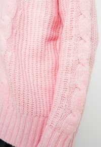 Ανοιχτό ροζ πλεκτό πουλόβερ με ριμπ τελείωμα και σχέδια πλεξούδα στα μανίκια. Μαλακή υφή και άνετη εφαρμογή με ορατή ρ αφή.