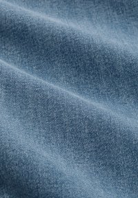 Material din denim albastru deschis cu textură diagonală vizibilă și pliuri moi.