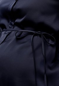 Tissu soyeux bleu marine foncé avec une fine ceinture nouée autour de la taille et un bouton visible sur un vêtement.