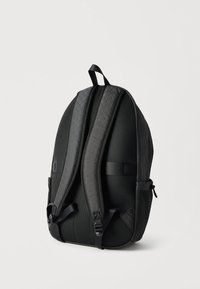 Μαύρο σακίδιο πλάτης με επενδεδυμένους ιμάντες ώμων και πλέγμα στο πίσω μέρος, από πίσω, σε απλό λευκό φόντο.