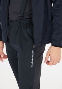 Veste navy avec des zips et un pantalon noir à taille élastique affichant "ENDURANCE" imprimé en blanc. Tissu lisse et léger, style ajusté.