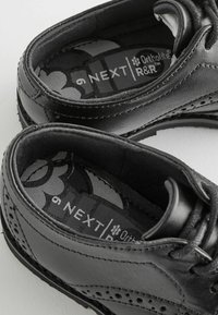Chaussures en cuir noir avec des détails brogue, dotées d'une semelle intérieure à motif étiquetée "Ortholite R&R." Texture lisse, bout arrondi et système de laçage.