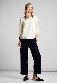 Blusa crema chiaro con scollo a V e maniche a tre quarti abbinata a pantaloni neri larghi e scarpe slip-on nere con dettagli in pelliccia.