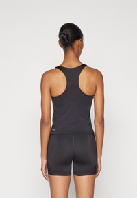 Fekete sportos tank top racerback kialakítással, fekete rövidnadrággal párosítva. Simább textúra, minimális varrásokkal, egy logóval az alján.