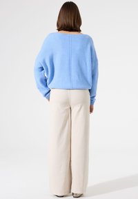 Pull bleu clair surdimensionné en matière douce, associé à un pantalon large crème, doté d'un tissu texturé et d'une coupe décontractée.