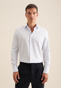 Witte blouse met een patroon, lange mouwen, knopen aan de voorkant en een kraag. Gecombineerd met donkere broek, die een nette pasvorm toont.
