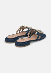 Denim slingback sandals with a low, square heel, featuring a jeweled embellishment on the upper and multiple cut-out straps.