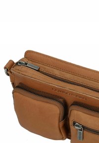 Borsa in pelle color mogano con diversi scomparti con zip, texture liscia e branding in rilievo, dotata di due piccole tasche frontali.