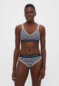 Ensemble bralette et culotte rayé bleu marine et blanc de Tommy Hilfiger, avec une ceinture logotée et des bretelles ajustables. Texture de tissu lisse.