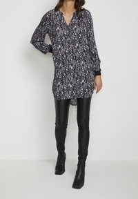 Tunique à imprimé floral aux tons foncés, avec col et devant boutonné ; associée à des leggings noirs brillants et des bottines.