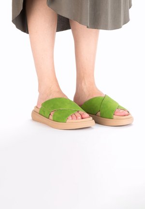 Green suede slide sandals with cross-over straps, light brown cushioned sole, and exposed toes. Simple design with no additional accents.