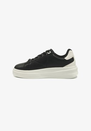Black leather sneaker with white heel accent and thick white sole, viewed from the side on a white background.